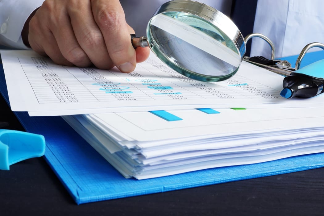 Tax auditor working on reports with magnifying glass